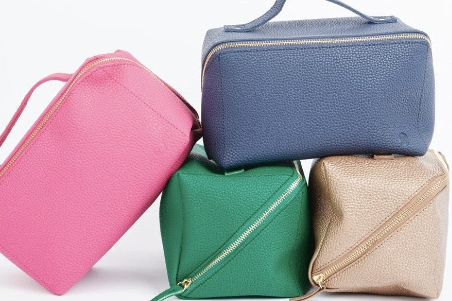 A collection of 4 makeup bags in pink, blue, green and gold on a white background