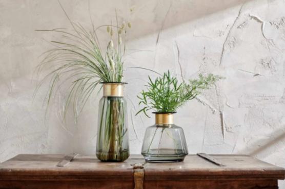 Two green and gold glass vases on a shelf with green stems