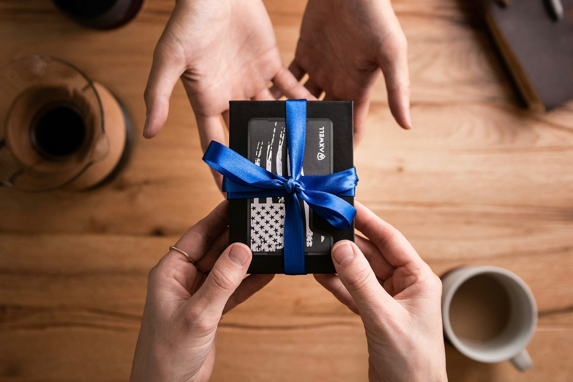 Two sets of hands handing over a gift wrapped box  with blue ribbon