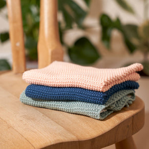 Stack of folded knitted clothes on a wooden chair with a blurred green plant background