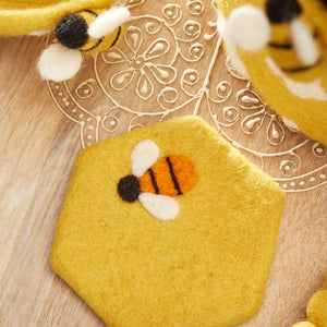 Hexagonal yellow felt piece with a bee design on a wooden surface.
