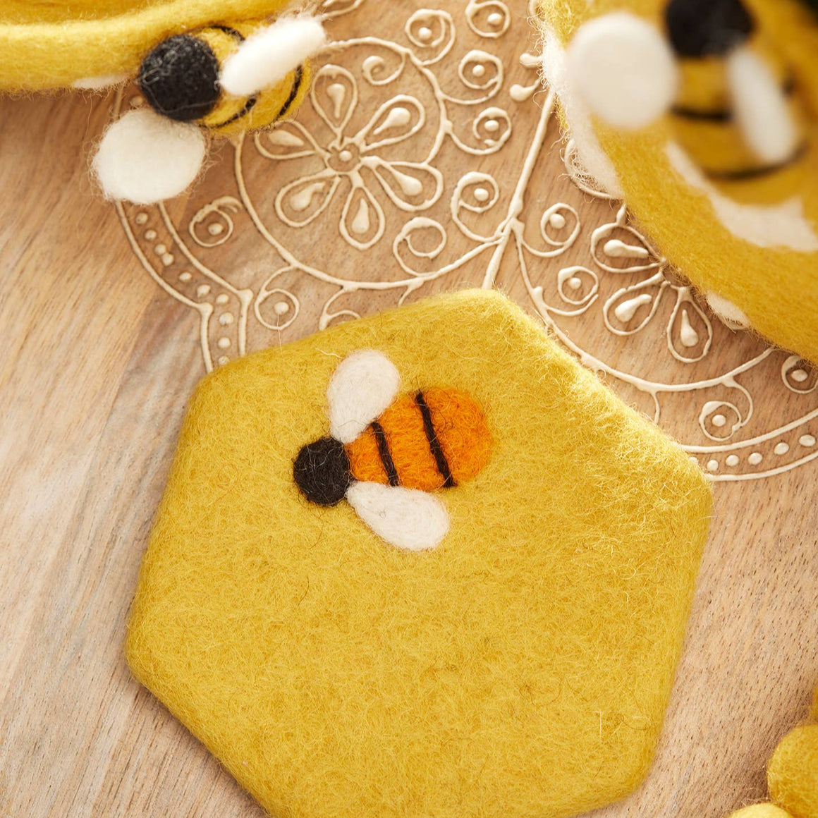 Hexagonal yellow felt piece with a bee design on a wooden surface.
