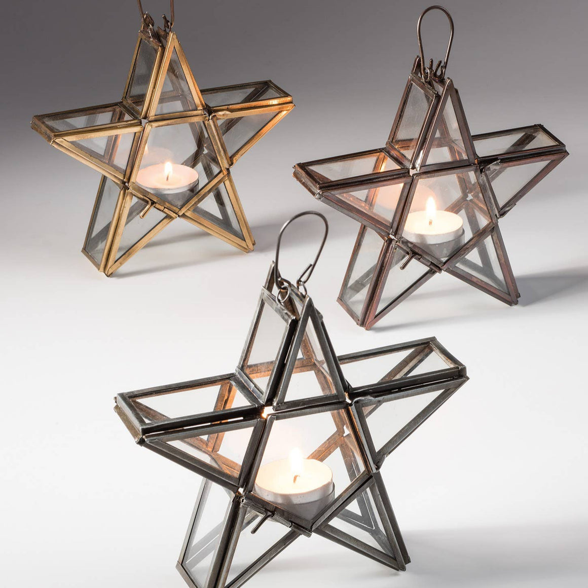 Star-shaped candle holders in gold, silver, and bronze on a gray background