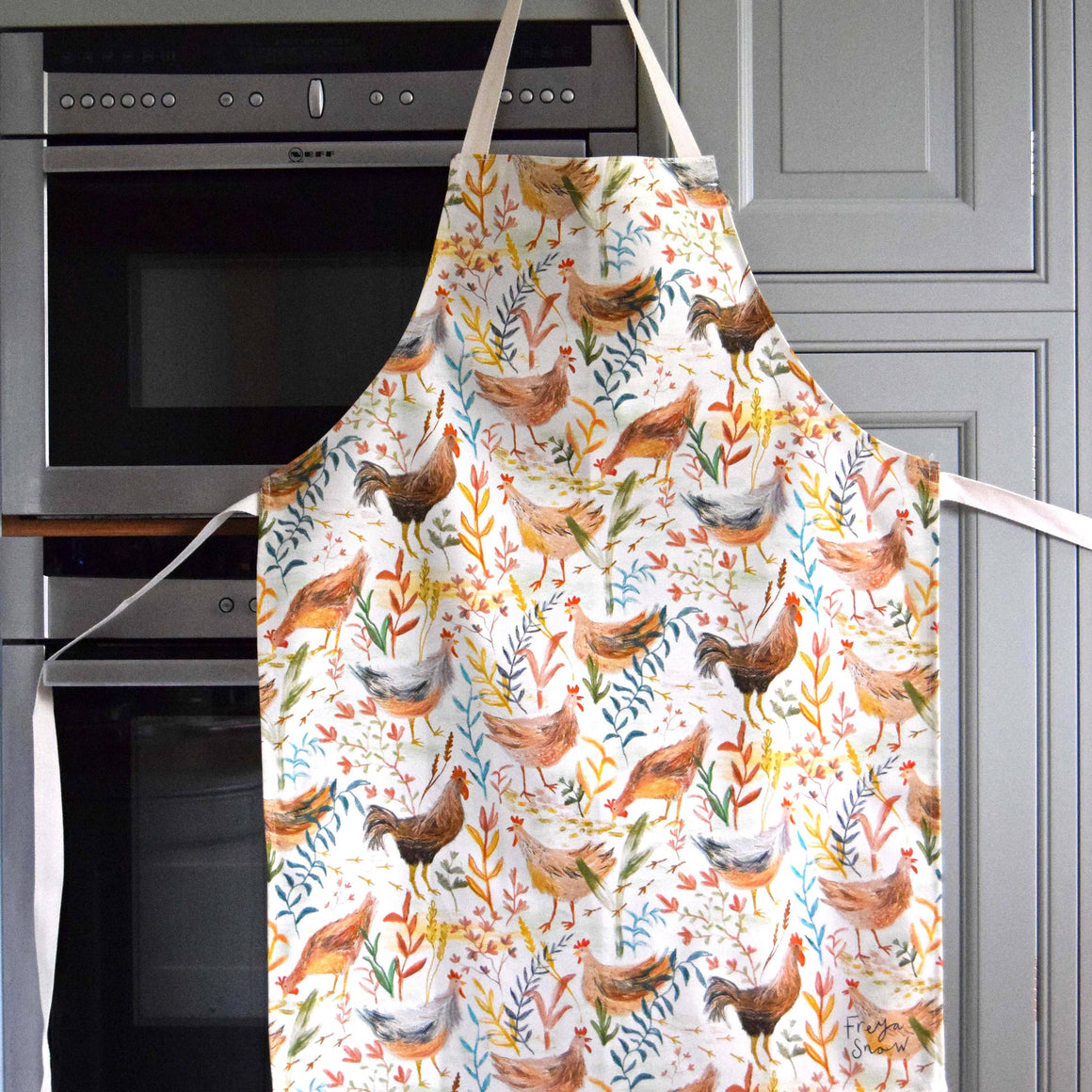 Colorful apron with chicken pattern hanging on a kitchen cabinet