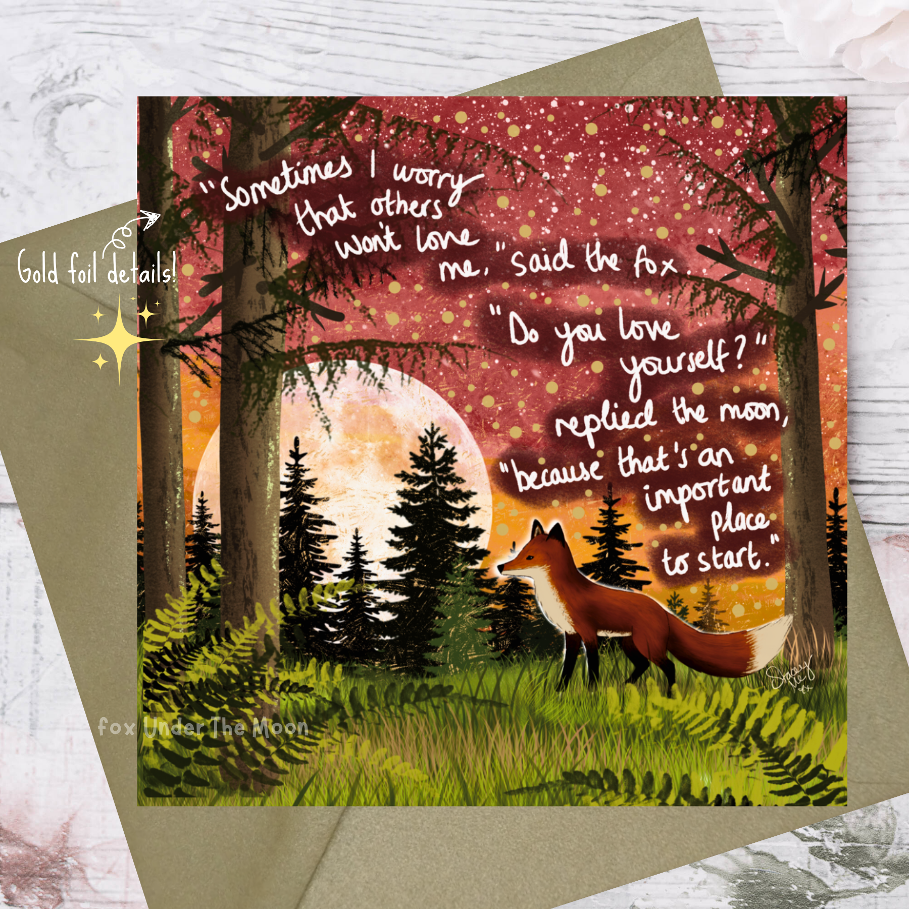 Greeting card with fox and moon illustration and inspirational quote on a wooden surface.
