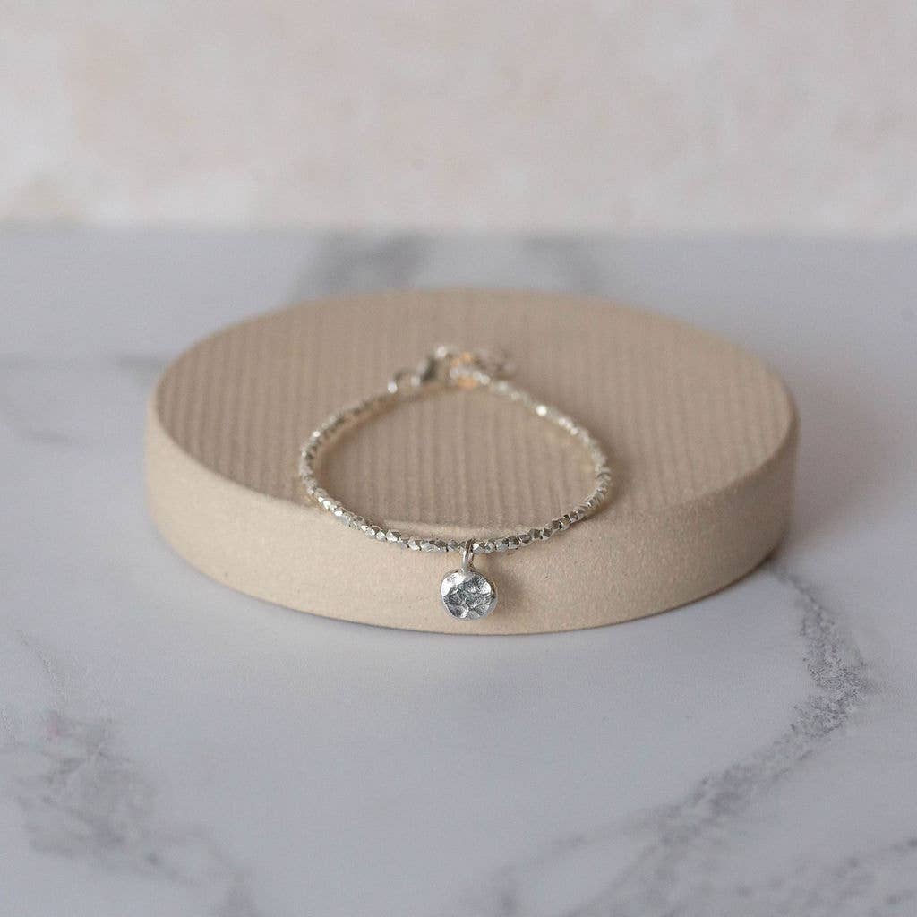 Silver bracelet with a small round charm on a beige stone surface