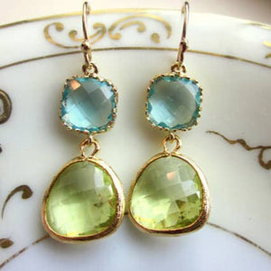 Gold earrings with green and blue gemstones on a decorative plate