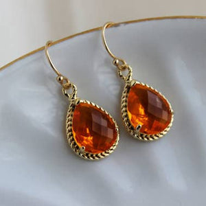 Gold earrings with orange gemstones on a white plate