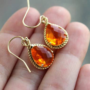Gold earrings with orange gemstones held in a hand against a blurred background