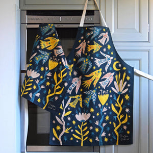 Decorative apron with a colorful design hanging on a kitchen cabinet.