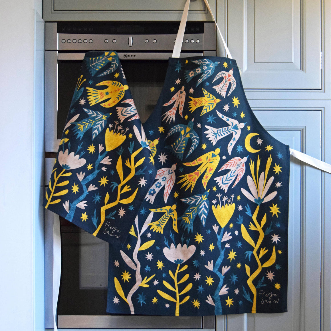 Decorative apron with a colorful design hanging on a kitchen cabinet.
