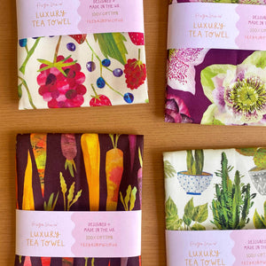 Set of four colorful tea towels with different patterns on a wooden surface.