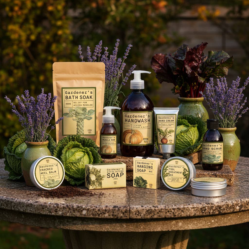 Collection of Gardener's products including soap, hand wash, and bath soak on a stone surface with plants in the background.
