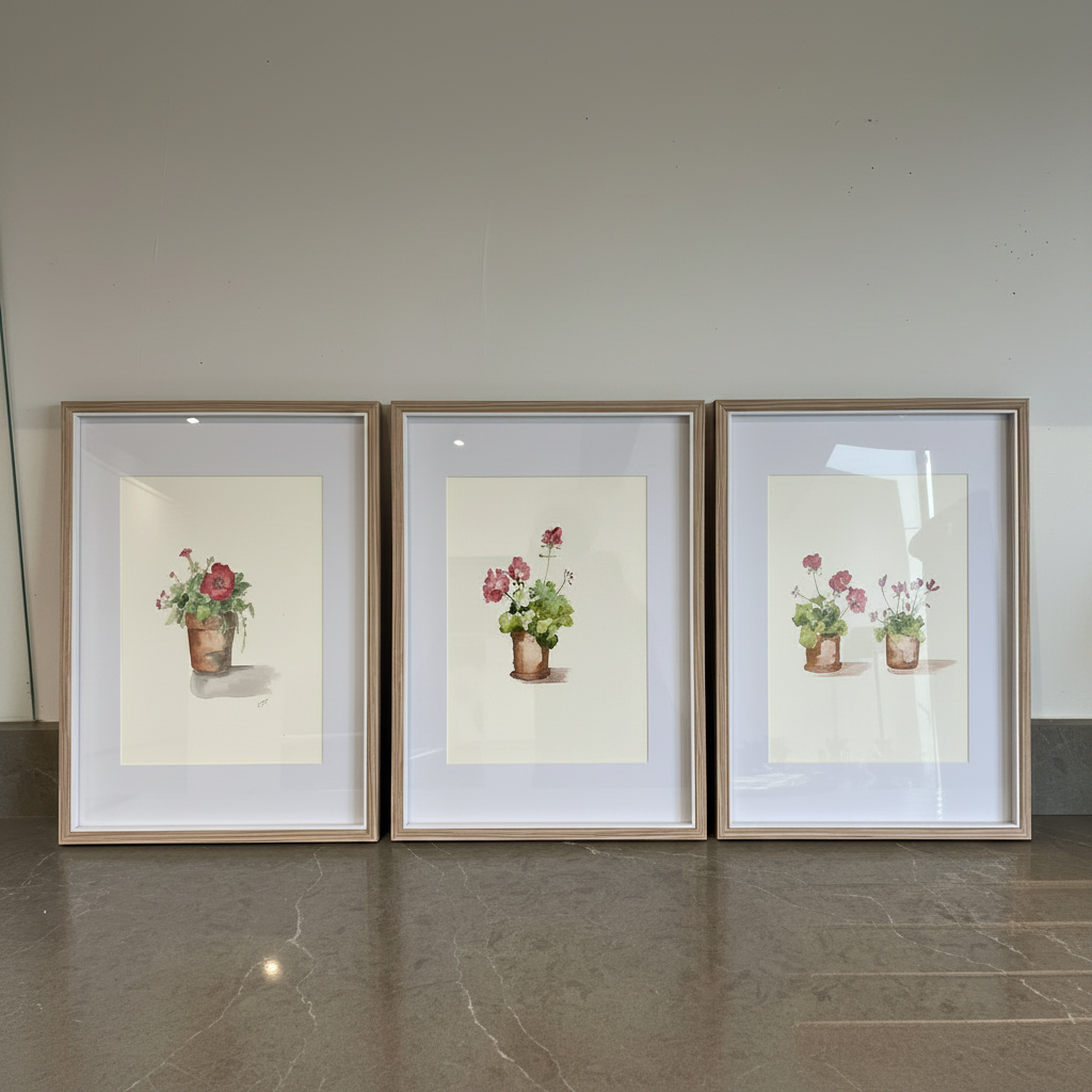 Three framed watercolor floral prints with potted flowers, displayed side-by-side on a polished stone floor against a plain wall.