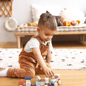 Child playing with a wooden toy train set on a wooden floor.