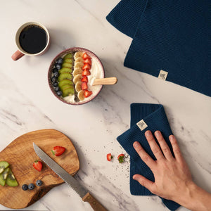 Napkin with brand logo on a marble surface with fruit salad and coffee.
