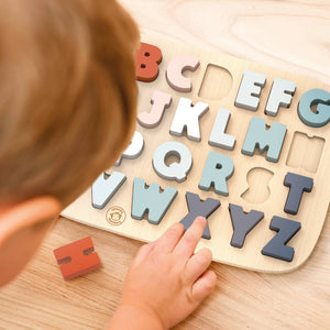 Child playing with a wooden alphabet puzzle on a wooden surface
