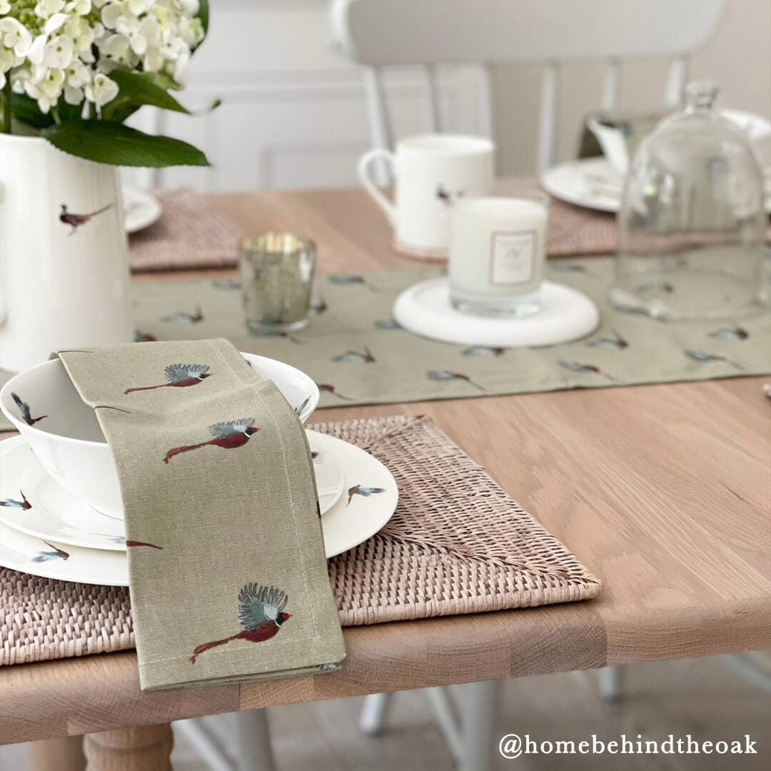 Dining table setting with embroidered runner and placemats featuring bird designs.