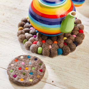 Colorful striped teapot on a wooden surface with a decorative trivet.