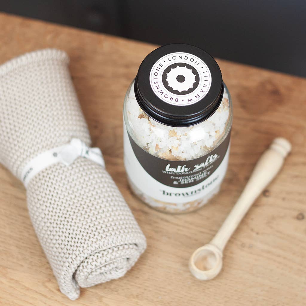 Jar of bath salts with a towel and spoon on a wooden surface