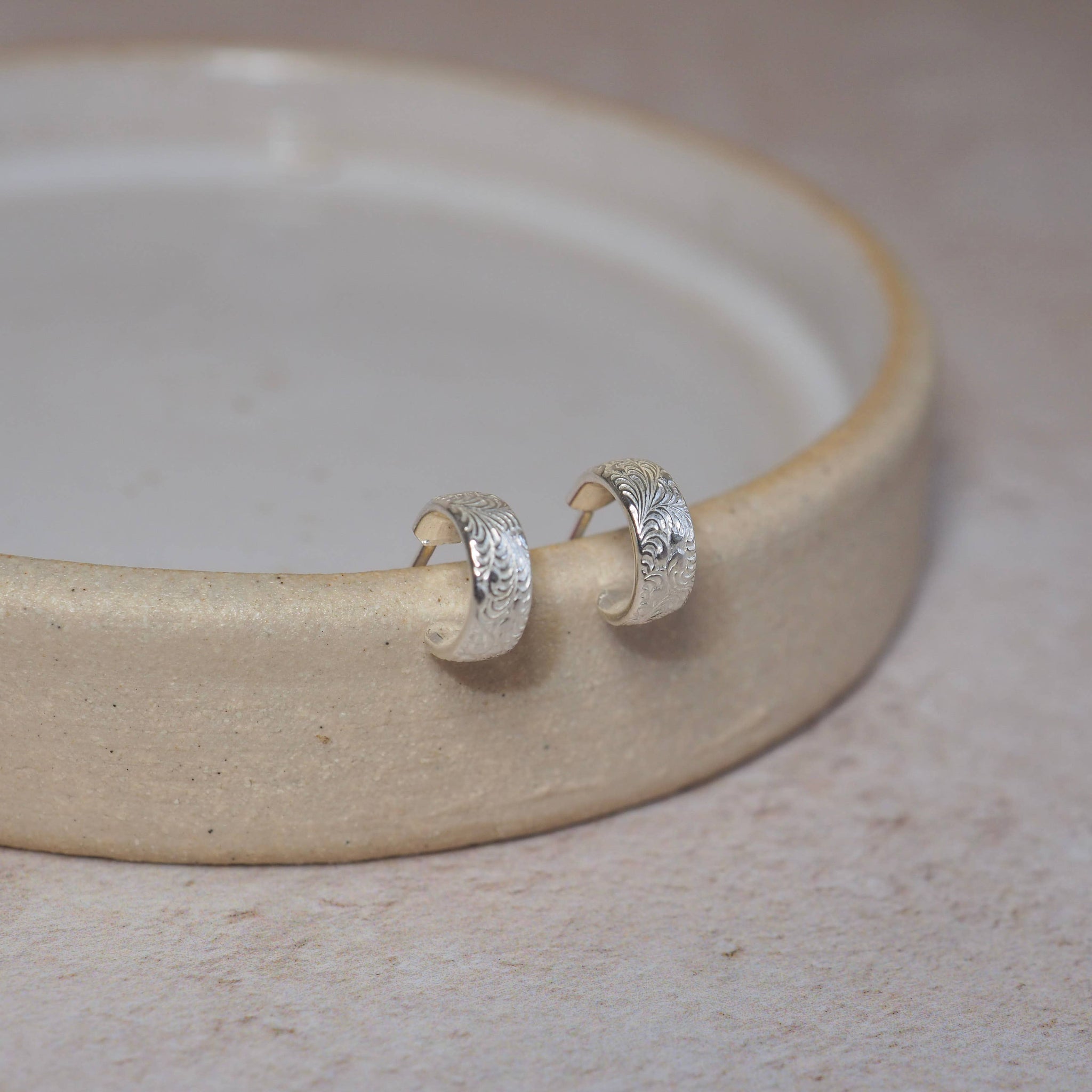 Silver hoop earrings on a beige ceramic dish