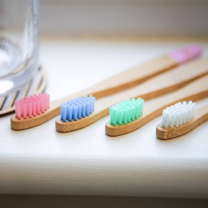 Set of four colorful bamboo toothbrushes on a light surface.