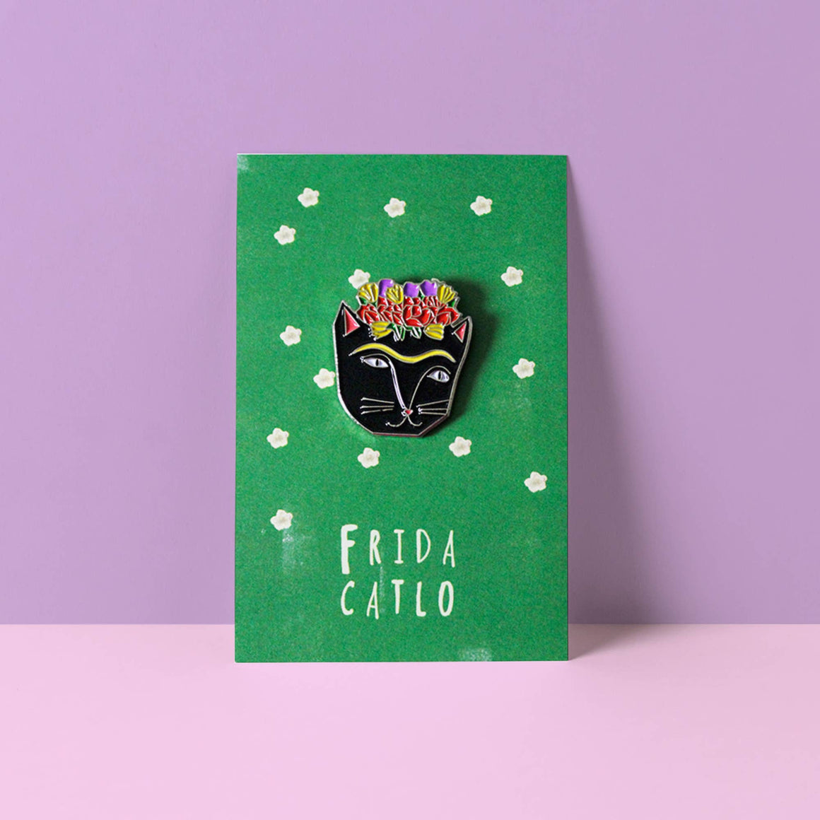 Frida Kahlo-themed pin on a green card with white flowers against a purple background