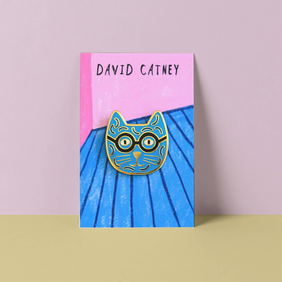 Cat-shaped pin with glasses on a blue and pink card with 'David Catney' text.
