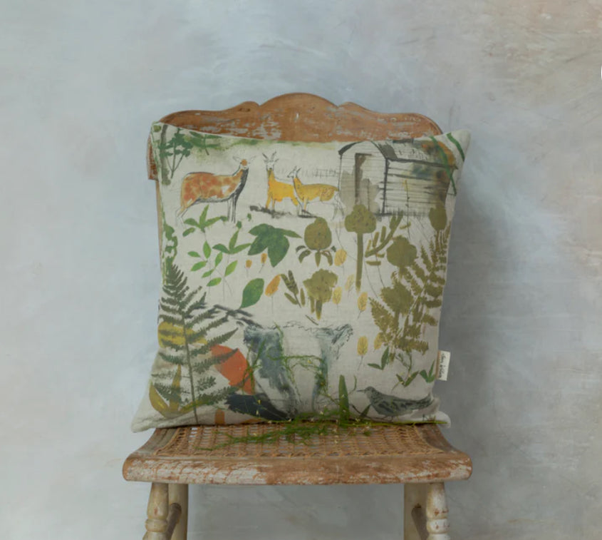 A square-shaped cushion with a nature and wildlife theme, featuring birds and foliage, placed on a neutral-toned sofa.