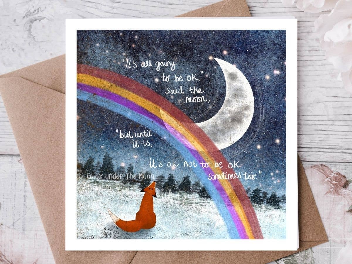 Card with a fox under a rainbow and moon, featuring motivational text on a wooden surface.