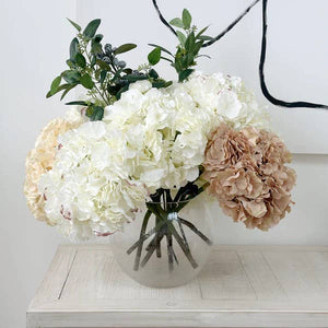 Bouquet of white and beige flowers in a clear vase on a wooden surface.