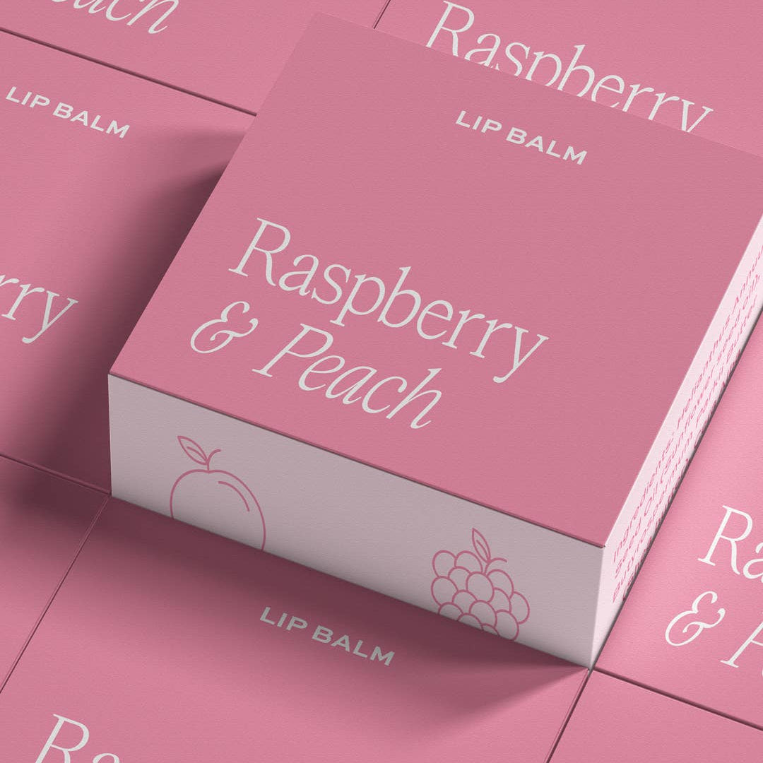 Raspberry and peach giftable lip balm by Moonshine Candle Co. in a sleek tube, featuring vibrant fruit-inspired packaging.