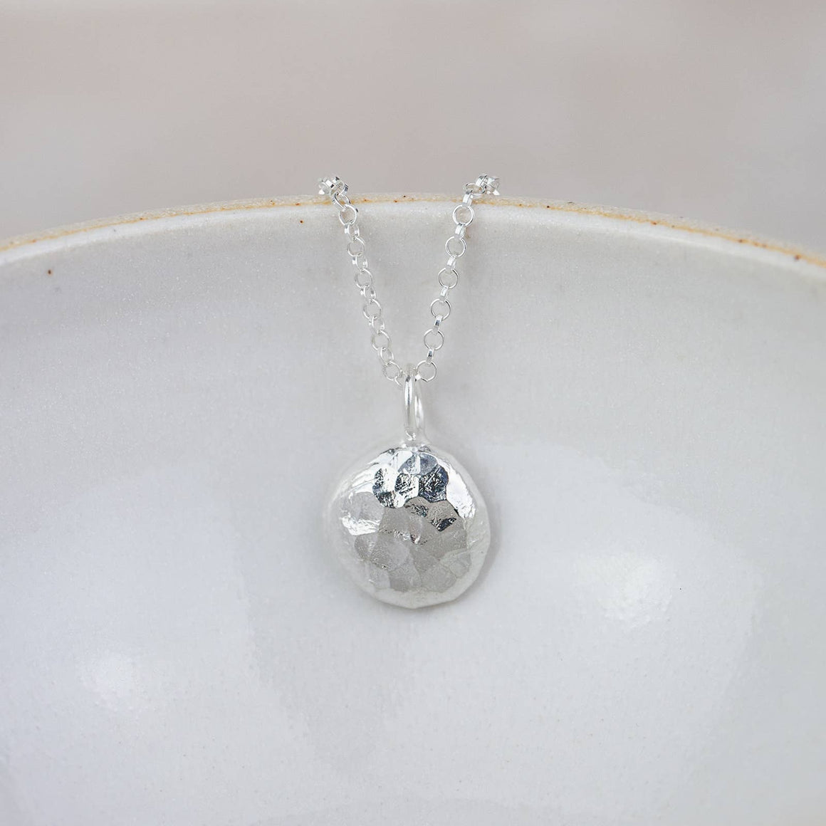 Silver necklace with a round pendant on a white dish