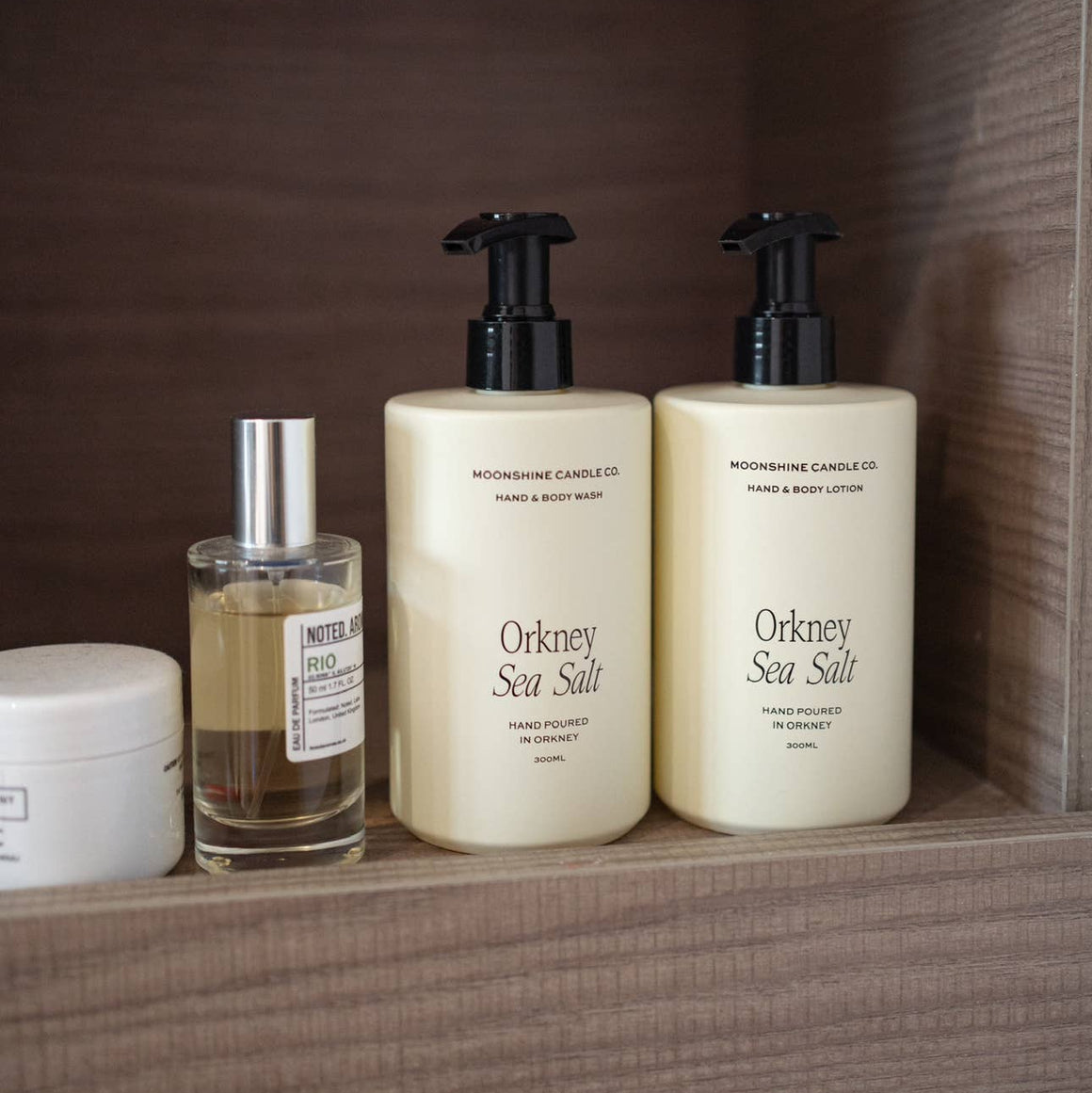 Three skincare products on a wooden shelf with a brown background