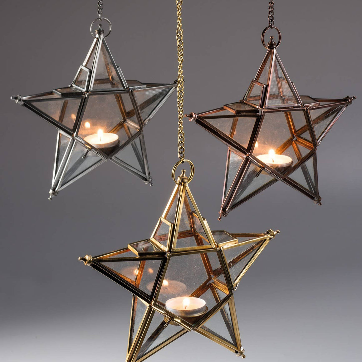 Three star-shaped glass lanterns hanging against a gray background