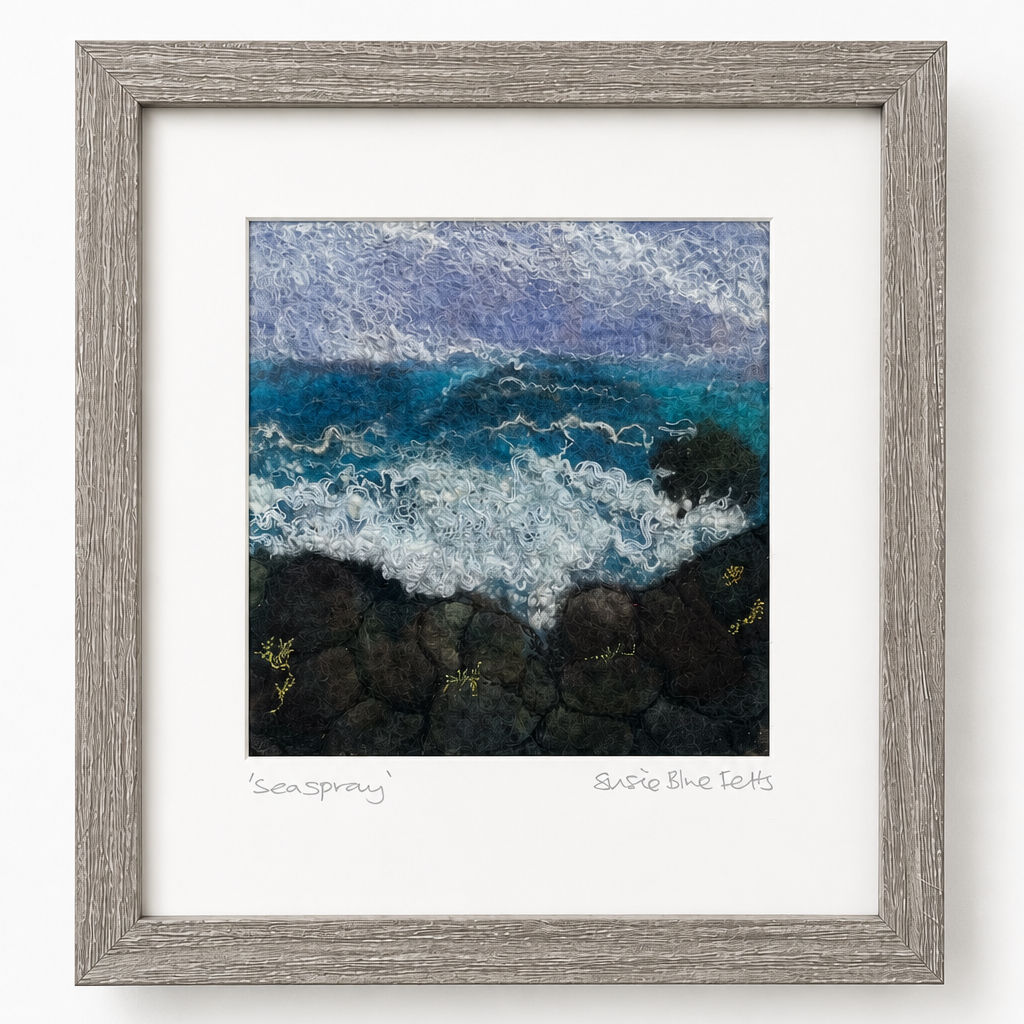 A framed art print depicting a textured, impressionistic seascape with blue and white waves crashing on dark rocks, set in a light gray wood frame with a white mat.