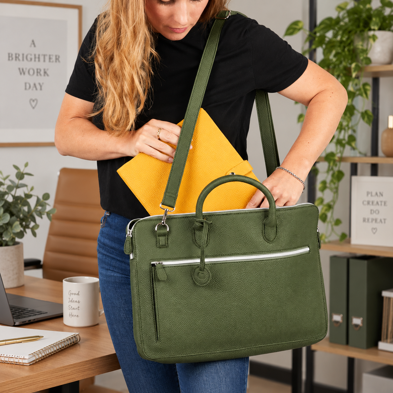 A woman in a black t-shirt and blue jeans carries an olive green textured leather briefcase with a top handle and shoulder strap in an office setting.
