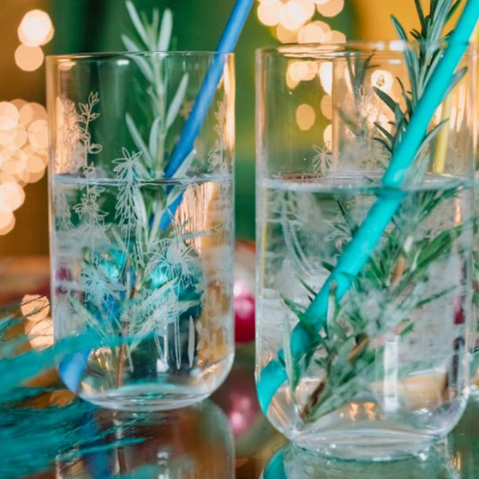 Etched glasses in floral design in a bar with rosemary and a straw