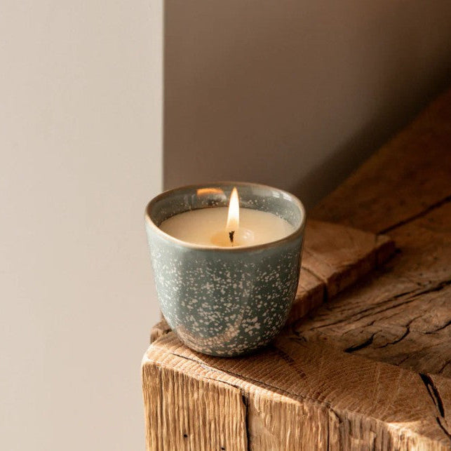 Ceramic candle holder with a lit candle on a wooden surface