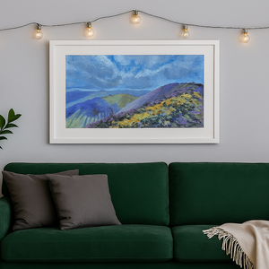 Framed landscape painting above a green sofa in a living room with string lights.