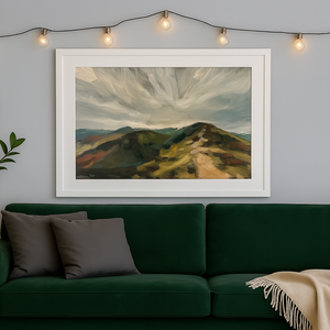 Framed landscape painting above a green sofa with string lights on the wall.