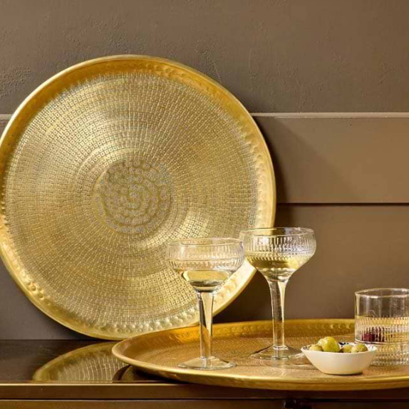 Gold decorative plate on a wooden surface with glasses and a bowl.