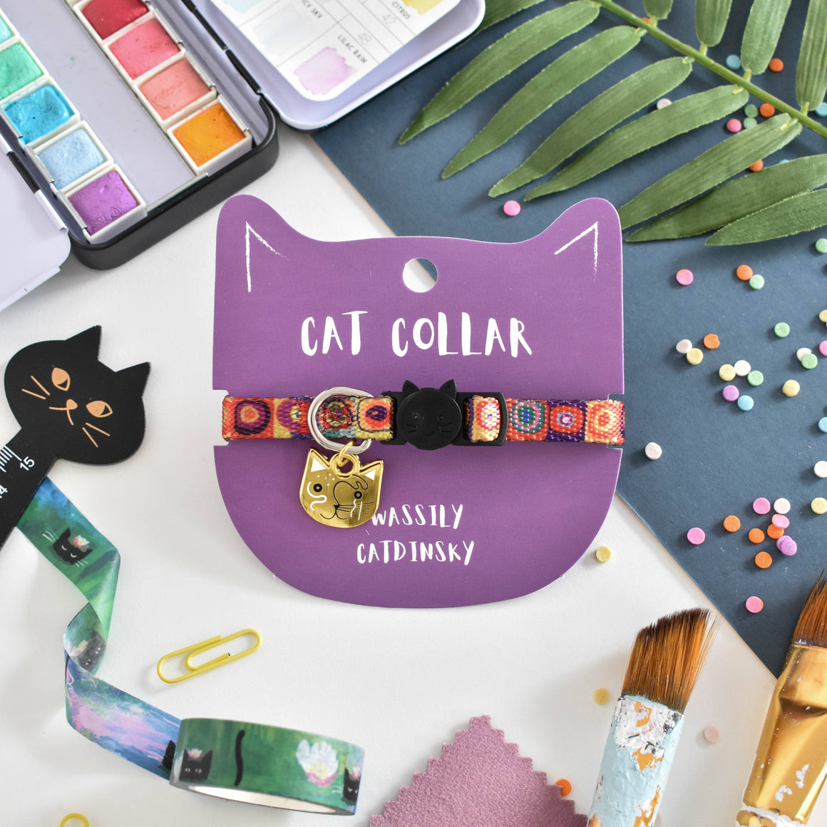 Cat collar with colorful design on a purple card, surrounded by art supplies on a blue background.