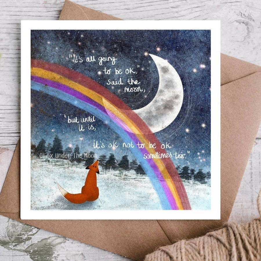 Card with a fox under a rainbow and moon, featuring motivational text on a wooden surface.