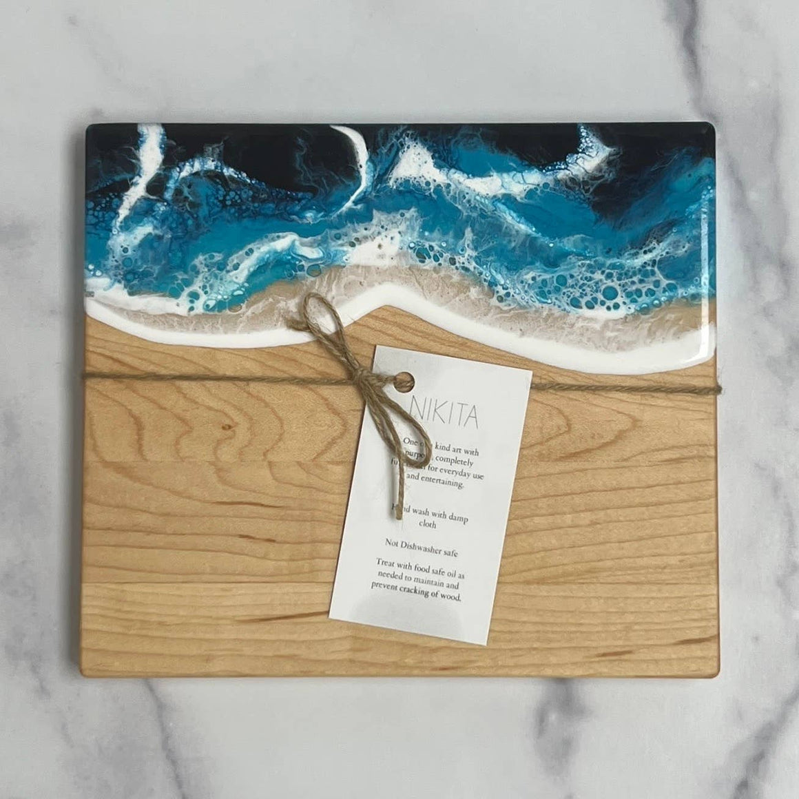 Wooden cutting board with ocean design and 'Nikita' tag on a marble background