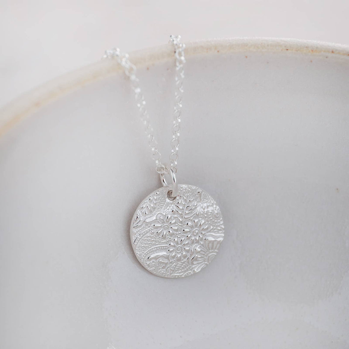 Silver necklace with a detailed circular pendant on a light background