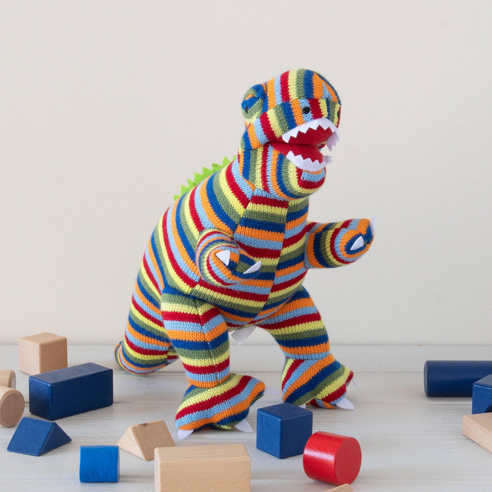 Colorful striped dinosaur toy among wooden blocks on a light wooden floor.