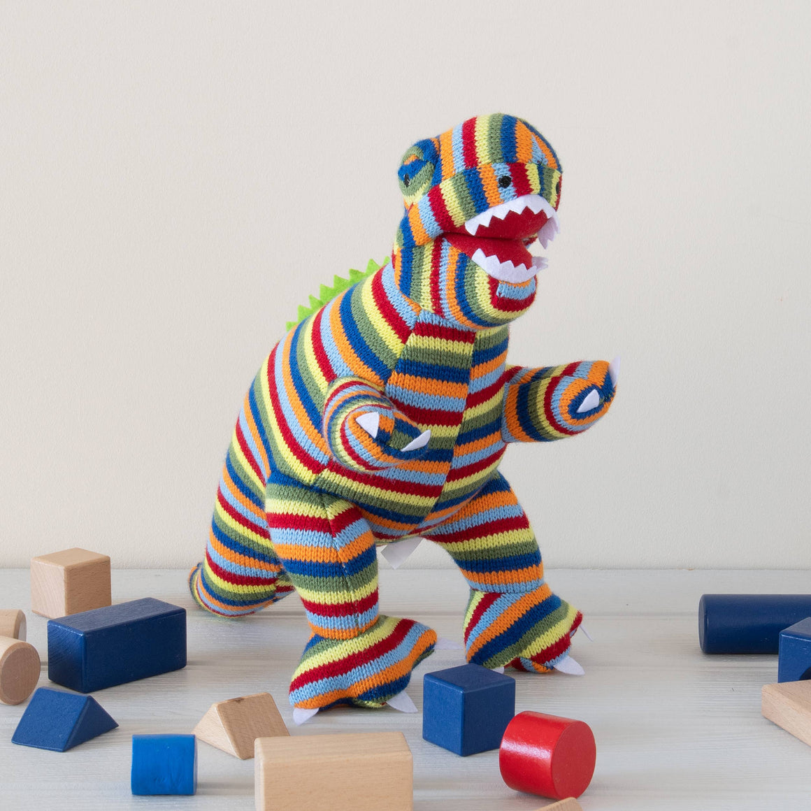 Colorful striped dinosaur toy among wooden blocks on a light wooden floor.