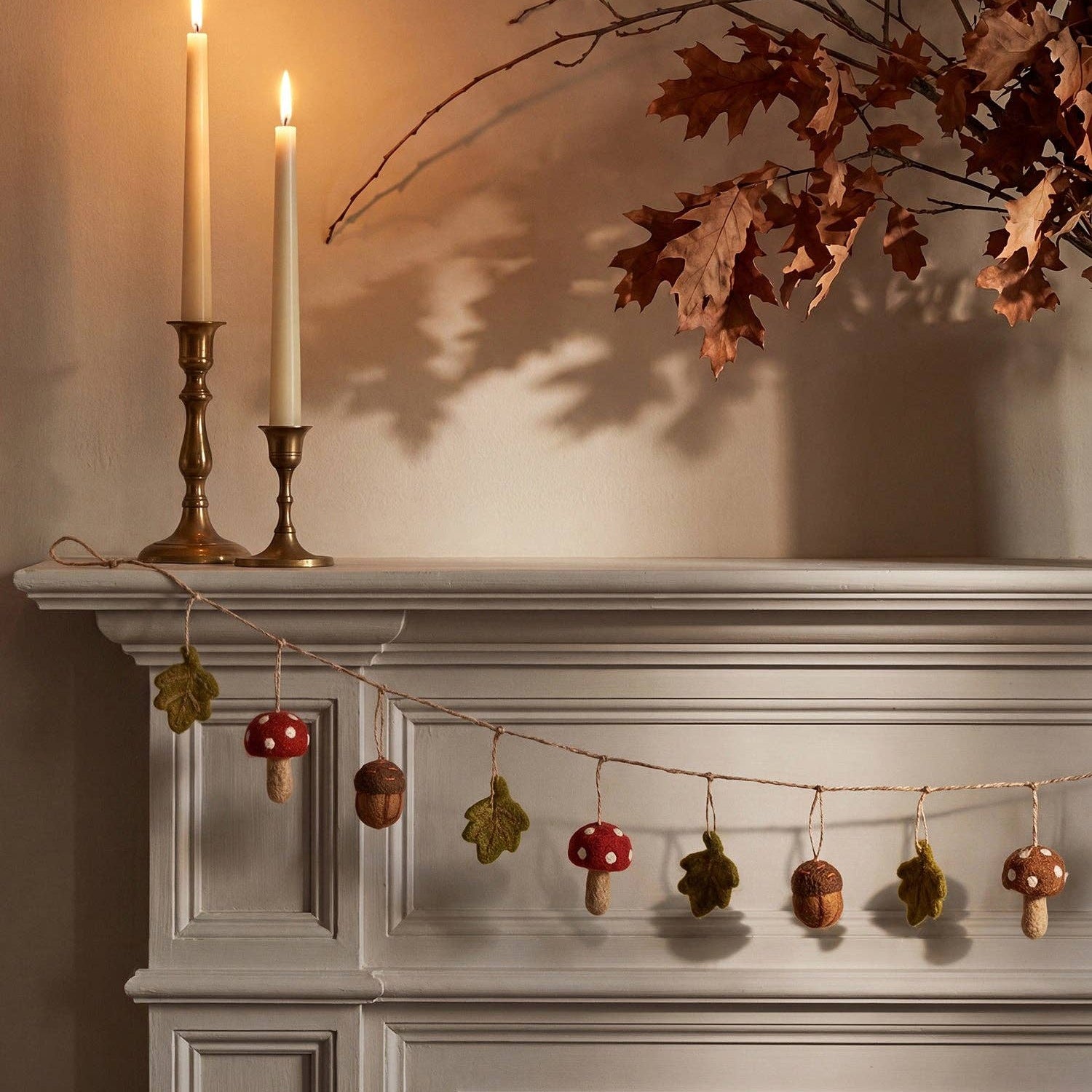 Decorative fireplace mantel with candles, leaves, and a string of small ornaments.
