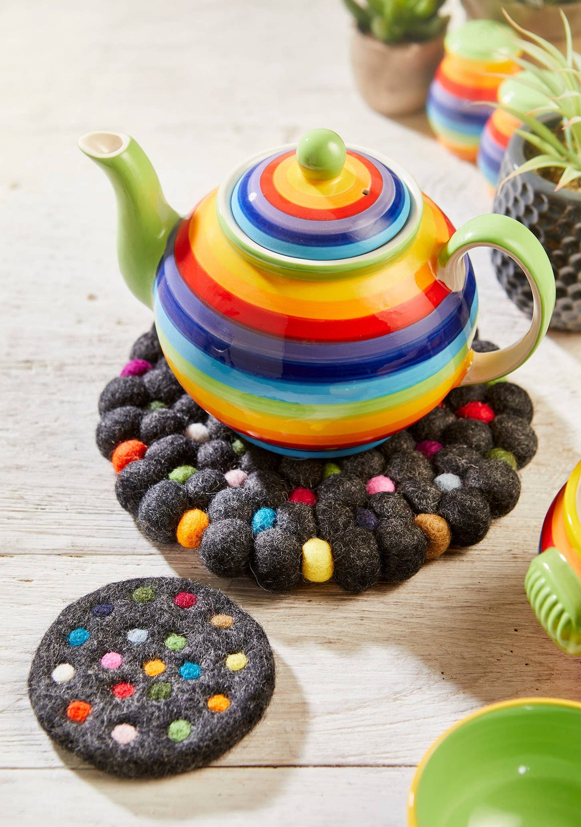 Colorful striped teapot on a wooden surface with a decorative trivet.